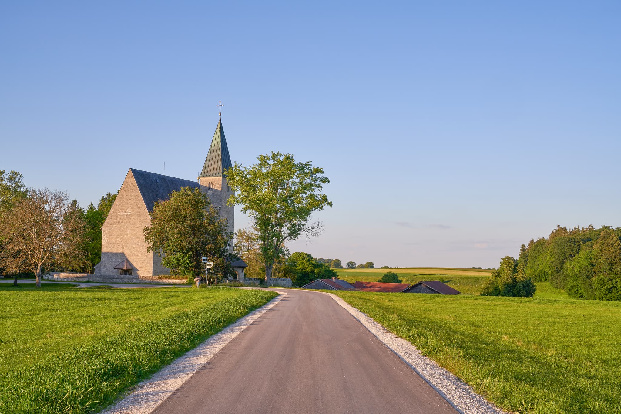 Die Kirche St. Pankratius in Meggenthal, Tittmoning, Traunstein, Oberbayern, Deutschland, ist von grünen Wiesen und einem Weg umgeben. Sie steht im Chiemgau.