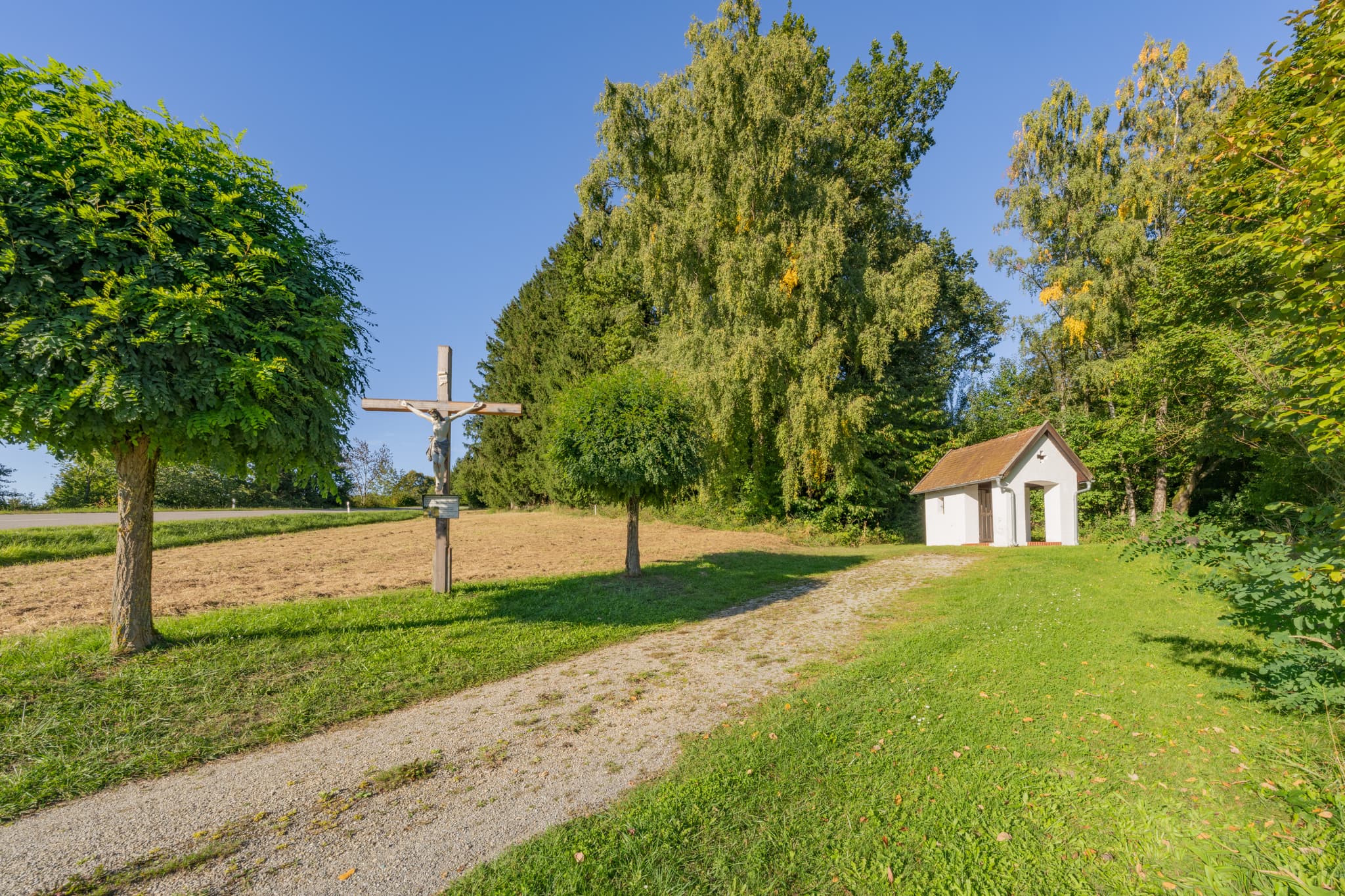 Bruder Konrad Kapelle und Wegkreuz in Hirschbach, Bad Birnbach. Landkreis Rottal-Inn, Niederbayern, Deutschland. Bäume, Felder, Wege im Bäderdrieck.