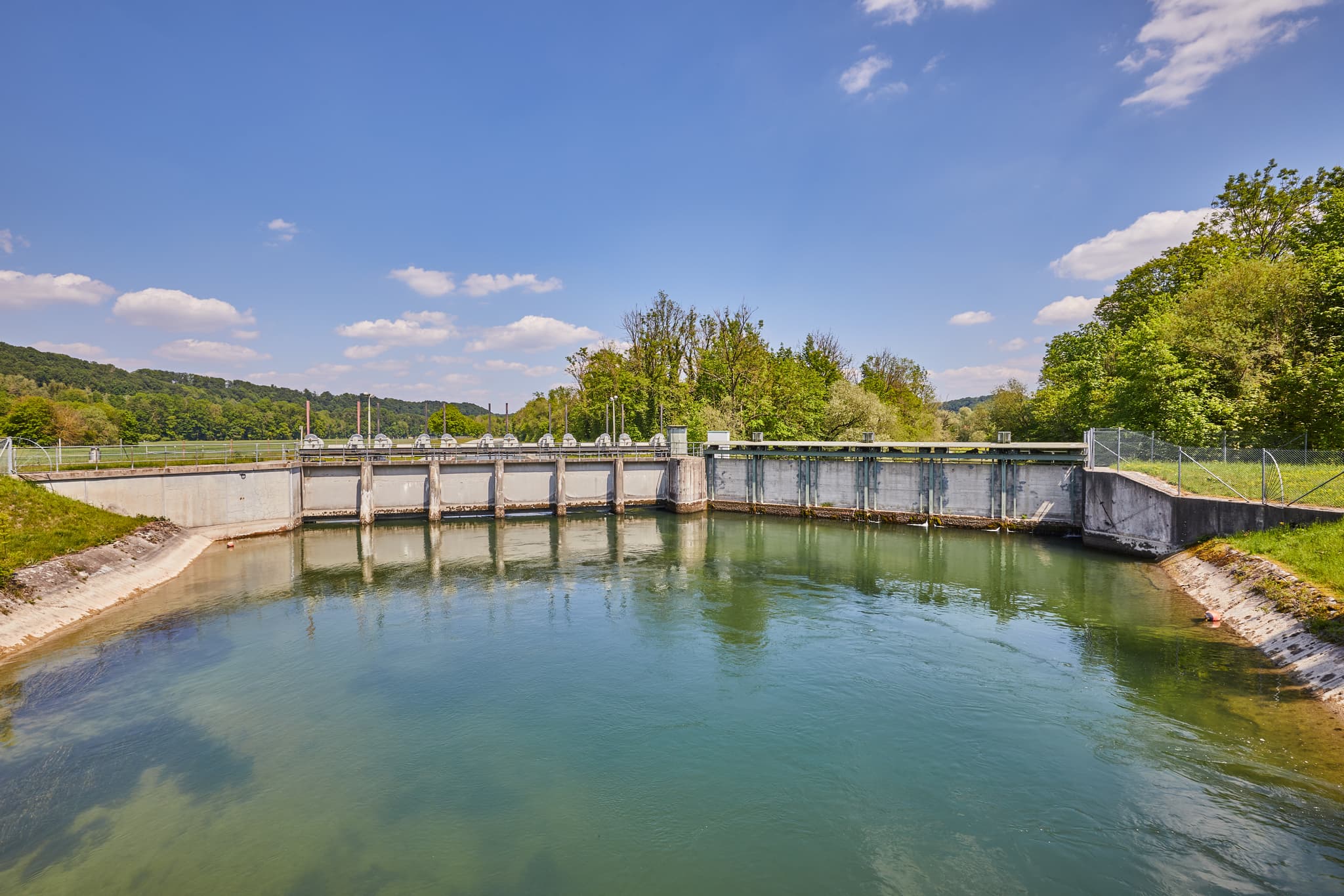 Ein Wehr am Alz Radweg in Burgkirchen, Altötting, Oberbayern, Inn-Salzach. Die Wasserlandschaft in Deutschland zeigt grüne Ufer, Bäume unter blauem Himmel.