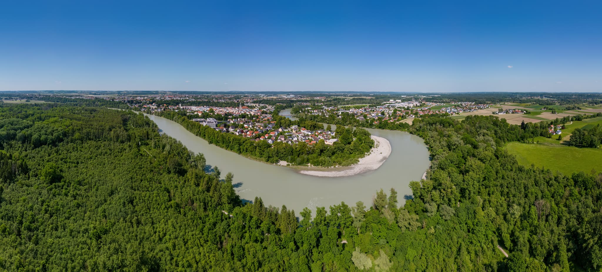 Luftbild von Mühldorf am Inn in Oberbayern, Deutschland. Der Inn schlängelt sich durch grüne Wälder. Im Hintergrund ist die Stadt Mühldorf zu sehen.