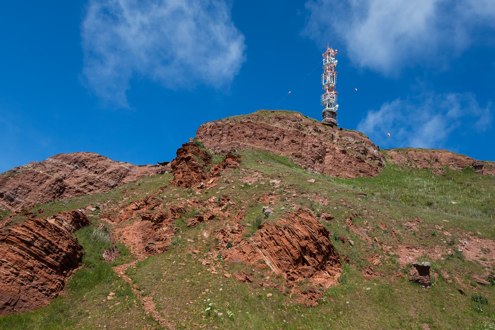 Funkturm auf rotem Felsenhügel mit grüner Vegetation. Aufgenommen in Helgoland Unterland, Helgoland, Kreis Pinneberg, Schleswig-Holstein, Nordsee, Deutschland.