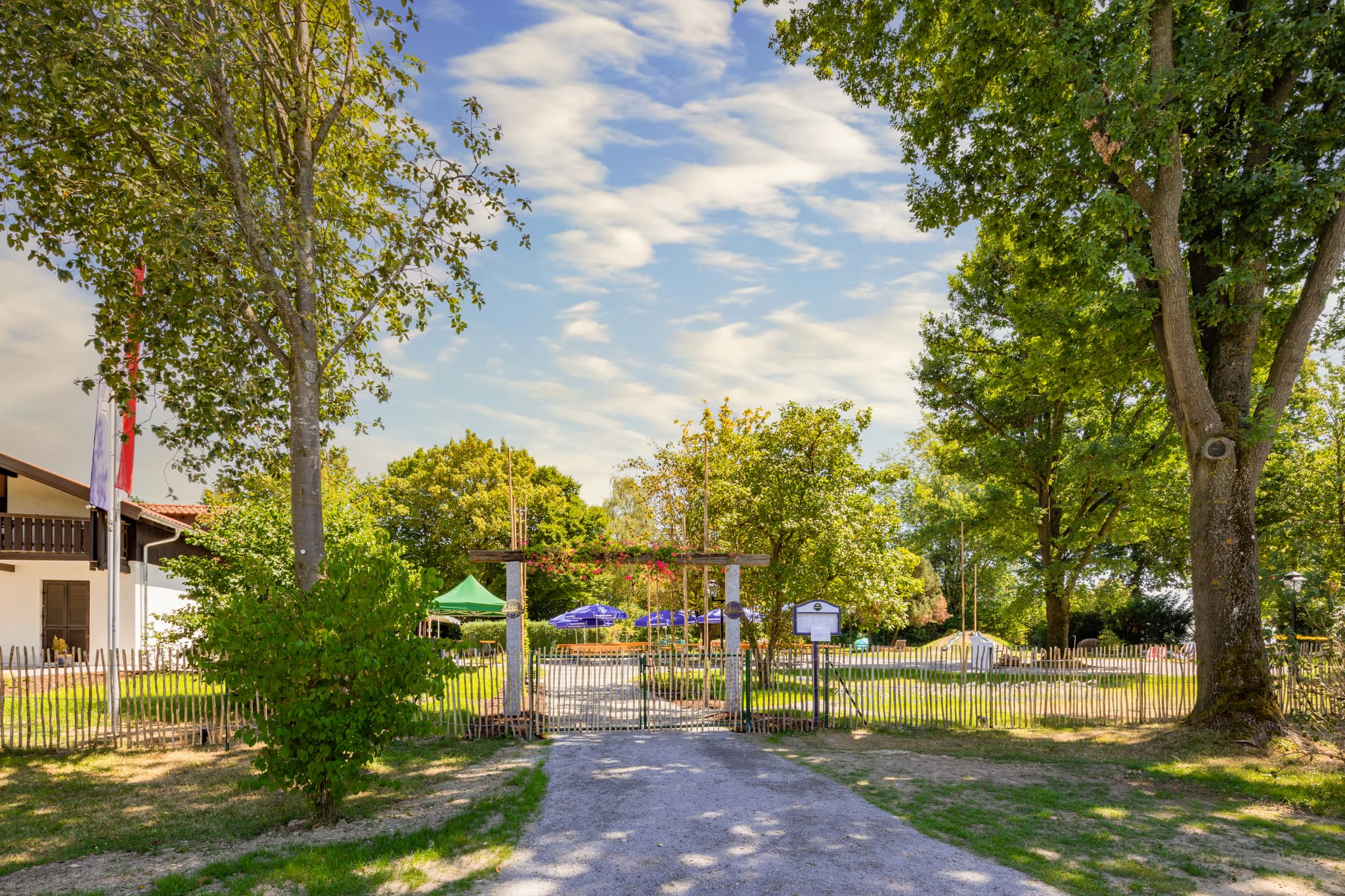 Biergarten im Kurpark von Bad Griesbach, Landkreis Passau. Das Bild zeigt den Eingangsbereich des Biergartens, umgeben von Bäumen und Grünflächen.