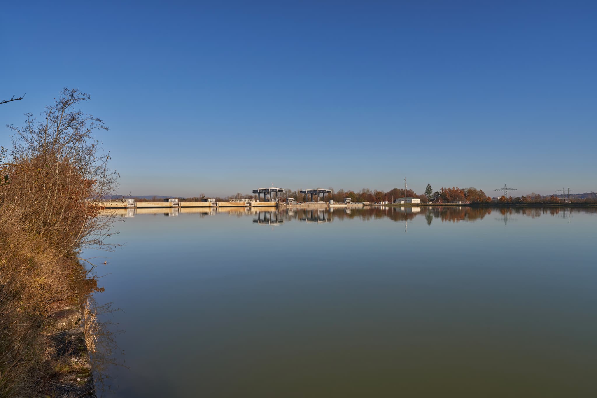 Blick auf Kraftwerk Simbach-Braunau bei Kirchdorf am Inn, Rottal-Inn, Niederbayern. Die Anlage am Inn spiegelt sich im ruhigen Gewässer wider.