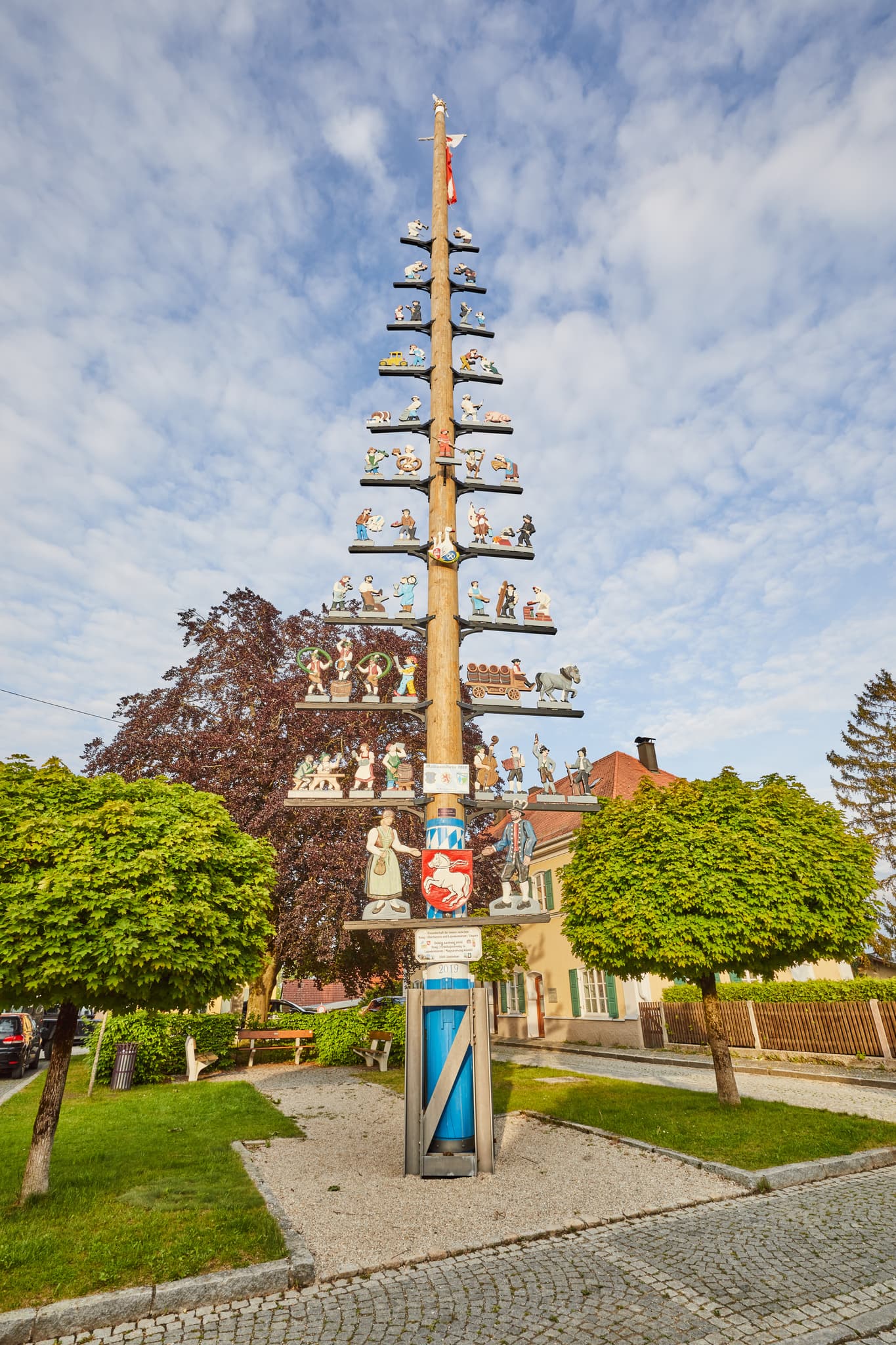 Ein festlich geschmückter Maibaum in Haag, Landkreis Mühldorf am Inn, Oberbayern, Region Inn-Salzach, Deutschland. Bei blauem Himmel und grünen Bäumen.