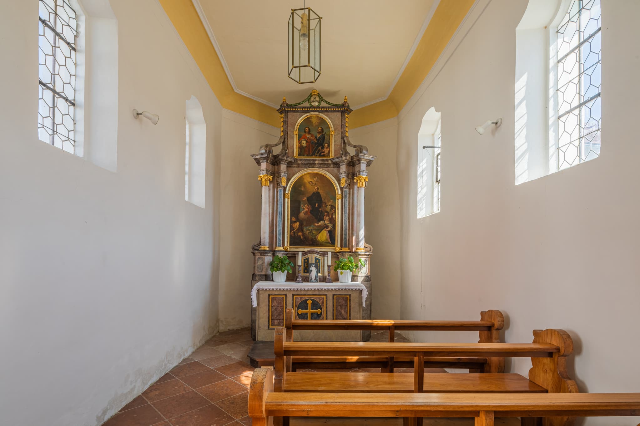 Innenansicht der Friedhofskapelle in Unterdietfurt, Landkreis Rottal-Inn, Niederbayern. Das Motiv zeigt den Altarbereich mit Holzbänken und Fenstern.