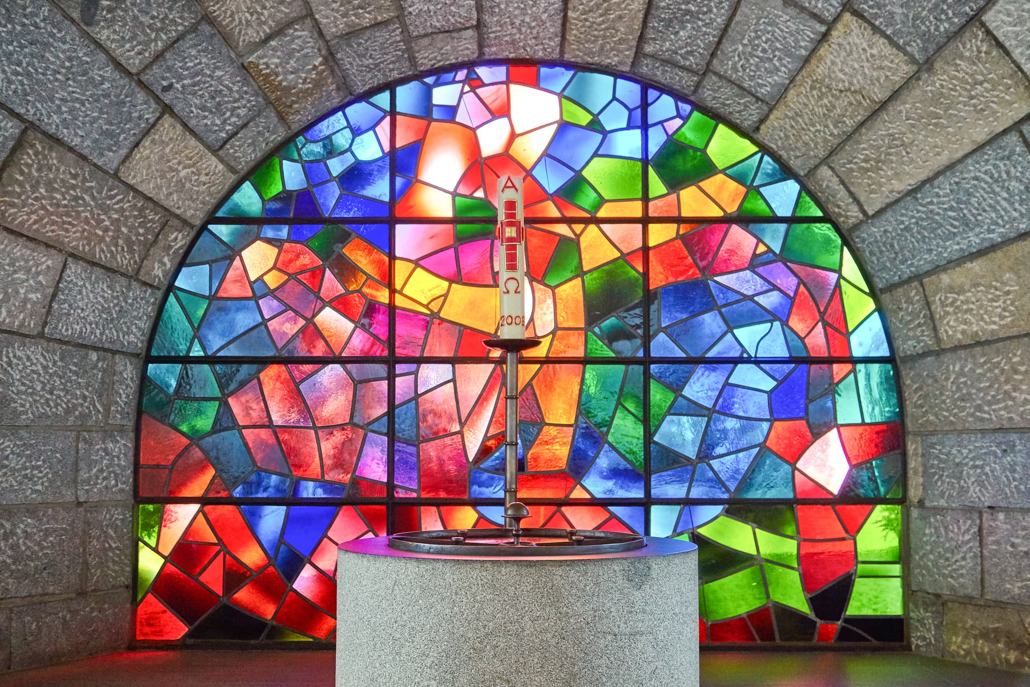 Farbenprächtiges Buntglasfenster der Pfarrkirche Heilig Geist in Bad Füssing, Landkreis Passau, Niederbayern. Taufstein, Region Donau-Wald, Deutschland.