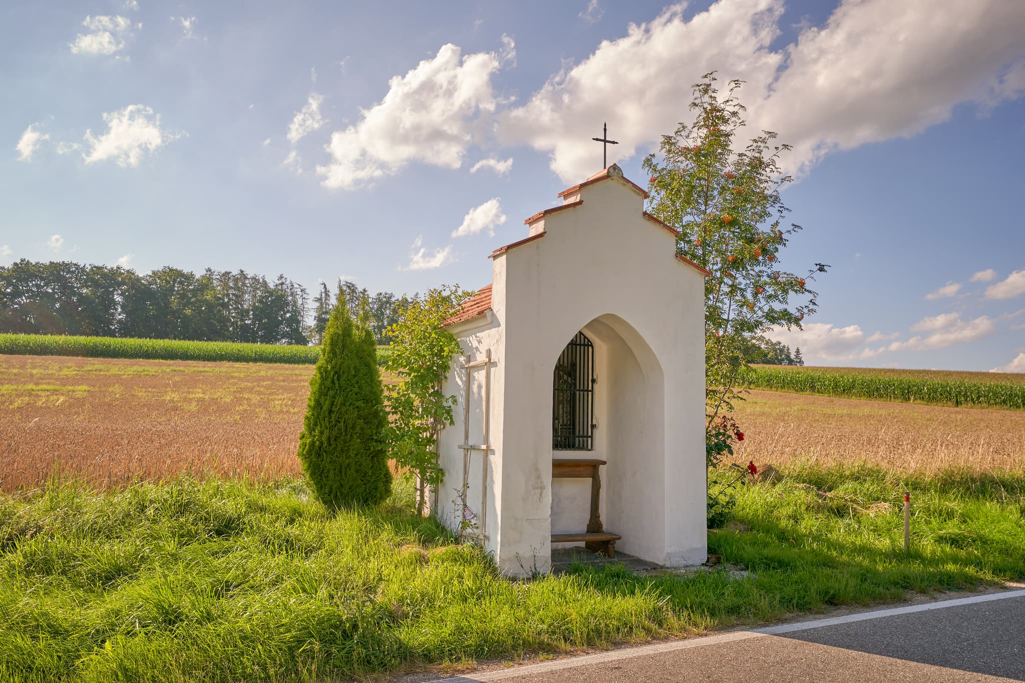 Bildstock am Feldrand in Niedertaufkirchen, Mühldorf am Inn, Oberbayern. Ländliche Szene Inn-Salzach, Deutschland, mit Feldern, Wiesen und blauem Himmel.
