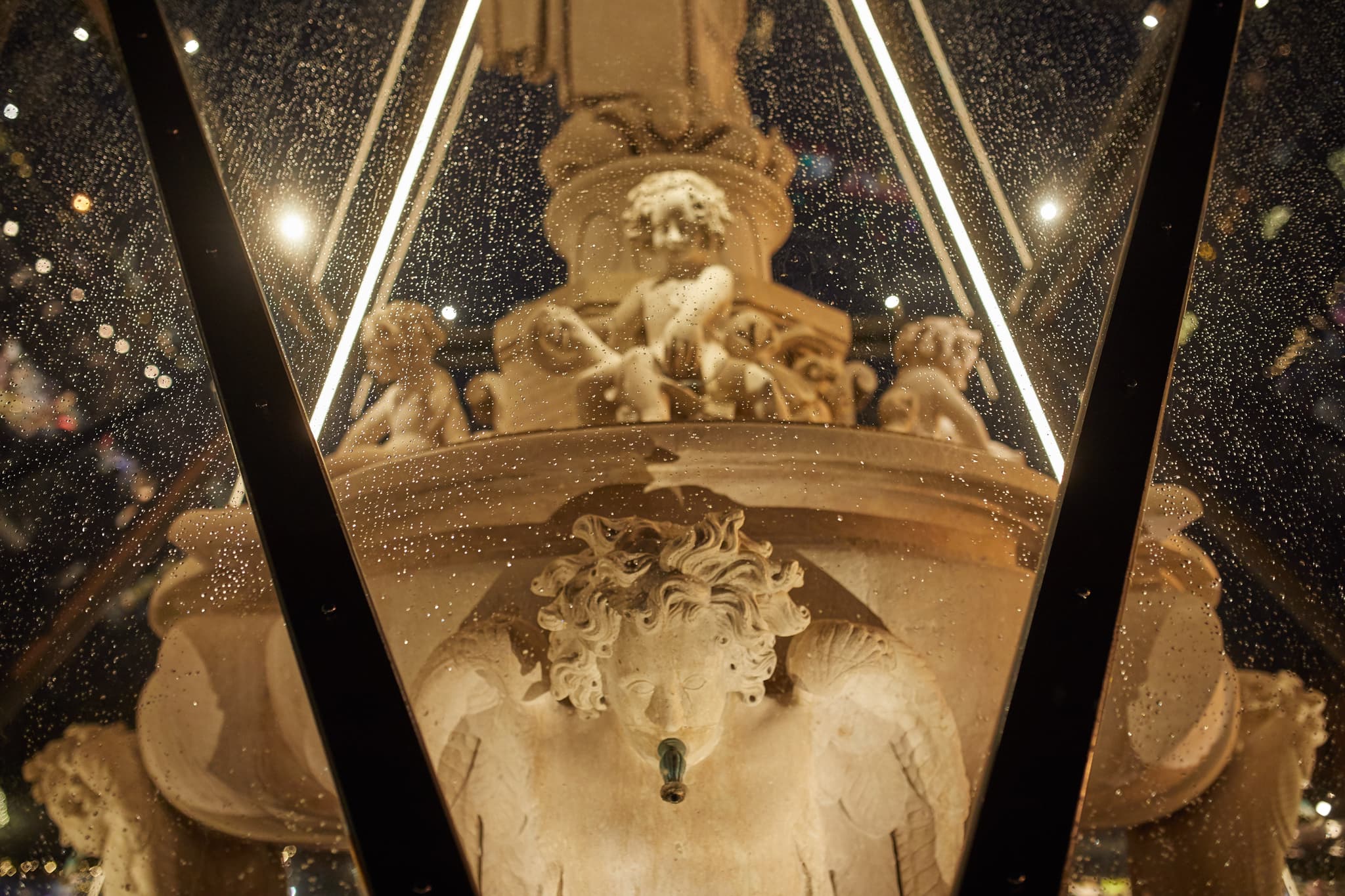 Der Kapellplatz Brunnen in Altötting, Landkreis Altötting, Oberbayern. Eine detaillierte Einhausung des historischen Brunnens ist bei Nacht beleuchtet.