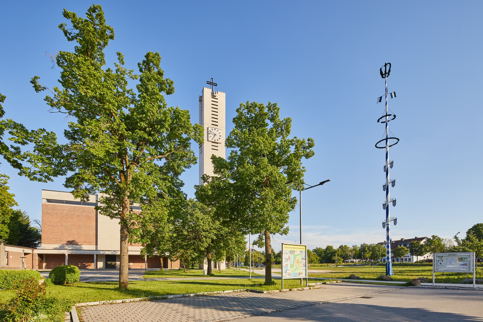 Die Pfarrkirche Heilig Geist in Emmerting, Altötting, Oberbayern, Inn-Salzach, Deutschland, zeigt ihren Kirchturm und  Maibaum unter blauem Himmel.
