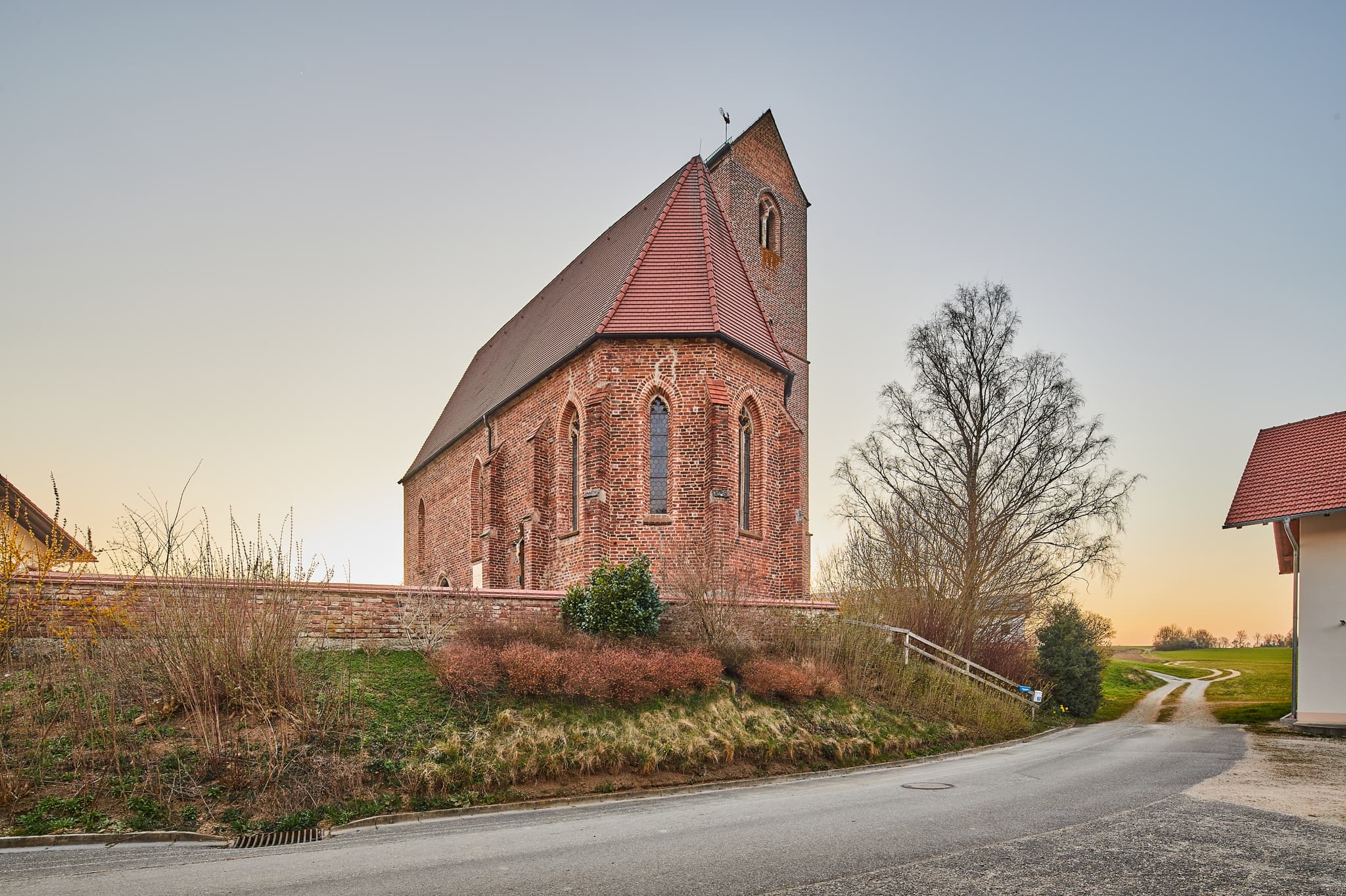 Gehersdorf Kirche in Zeilarn, Rottal-Inn, Niederbayern, Deutschland. Der Backstein-Bau steht in ländlicher Umgebung der Region Holzland. Ein Feldweg führt weg.