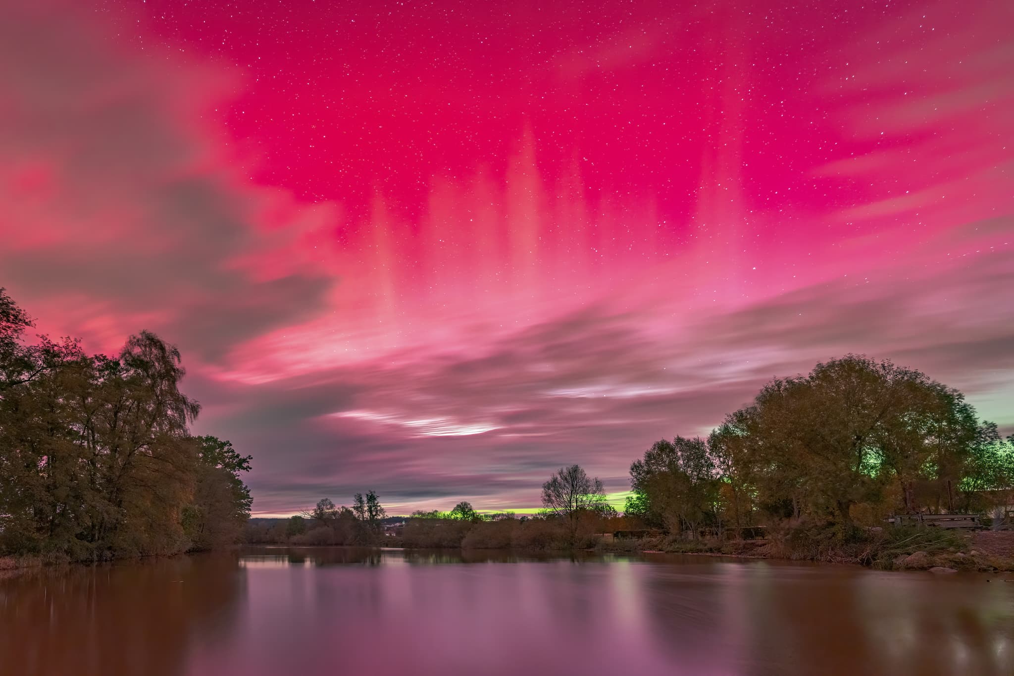 Beeindruckende Polarlichter am Himmel über dem Gewässer bei Voitl in der Au, Bayerbach. Seltenes Naturphänomen in Rottal-Inn, Niederbayern, Deutschland.