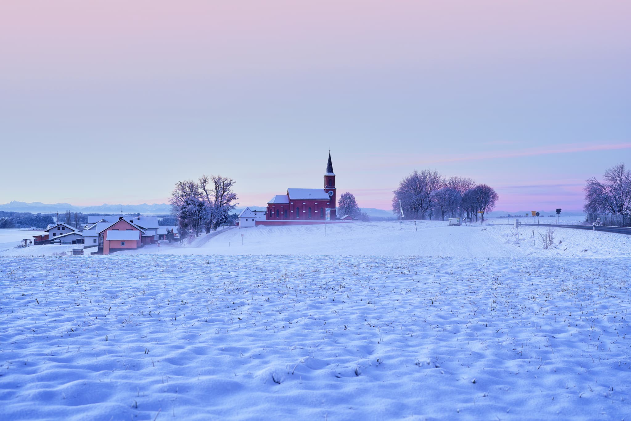 Winterlandschaft bei Wald bei Winhöring, Pleiskirchen, Altötting, Oberbayern. Verschneite Felder mit Kirche und Häusern in Region Inn-Salzach, Deutschland.