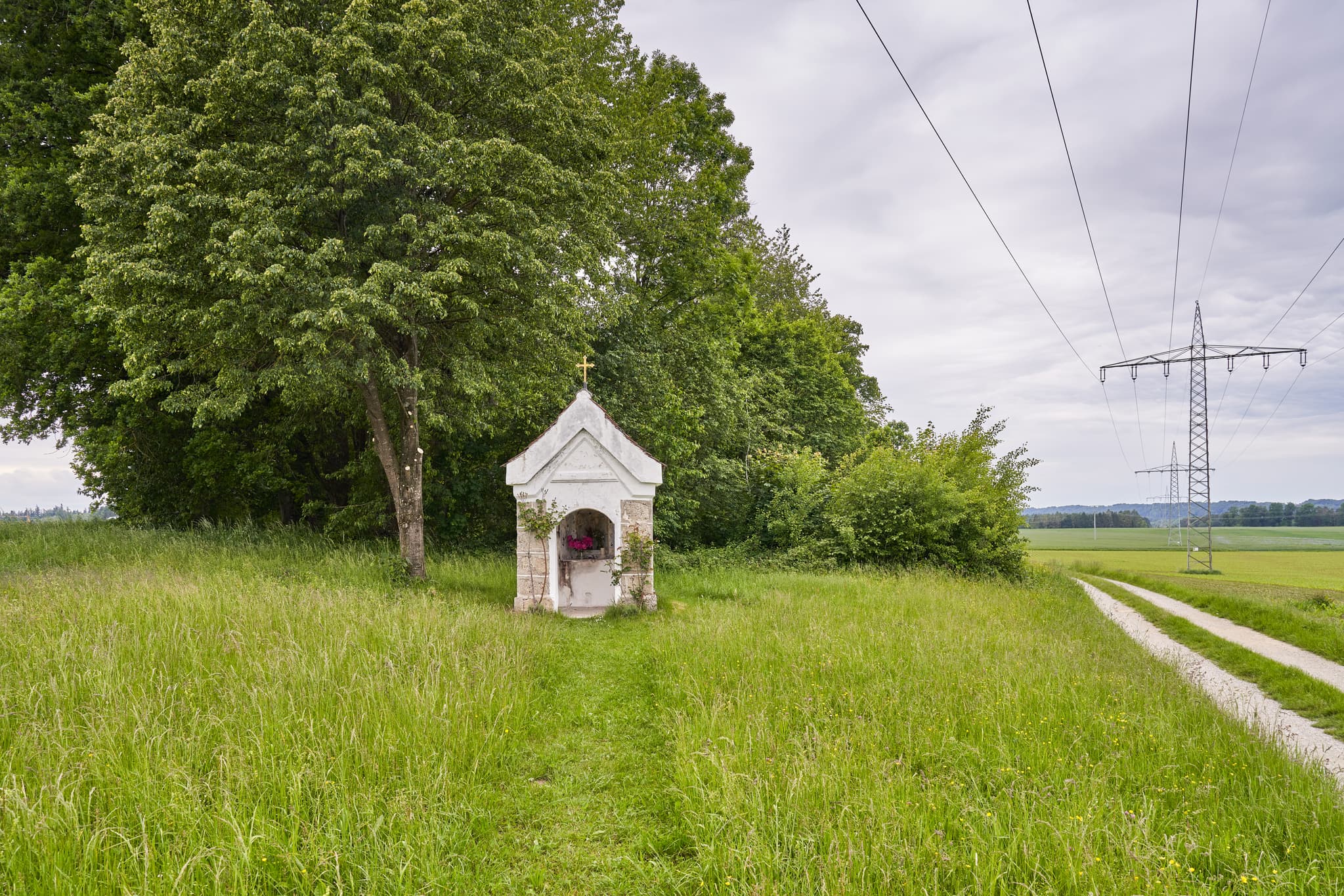 Ansicht einer Kapelle mit Marienstatue hinter Gitter und Blumen in Höresham, Burgkirchen. Im Landkreis Altötting, Oberbayern, Region Inn-Salzach, Deutschland.