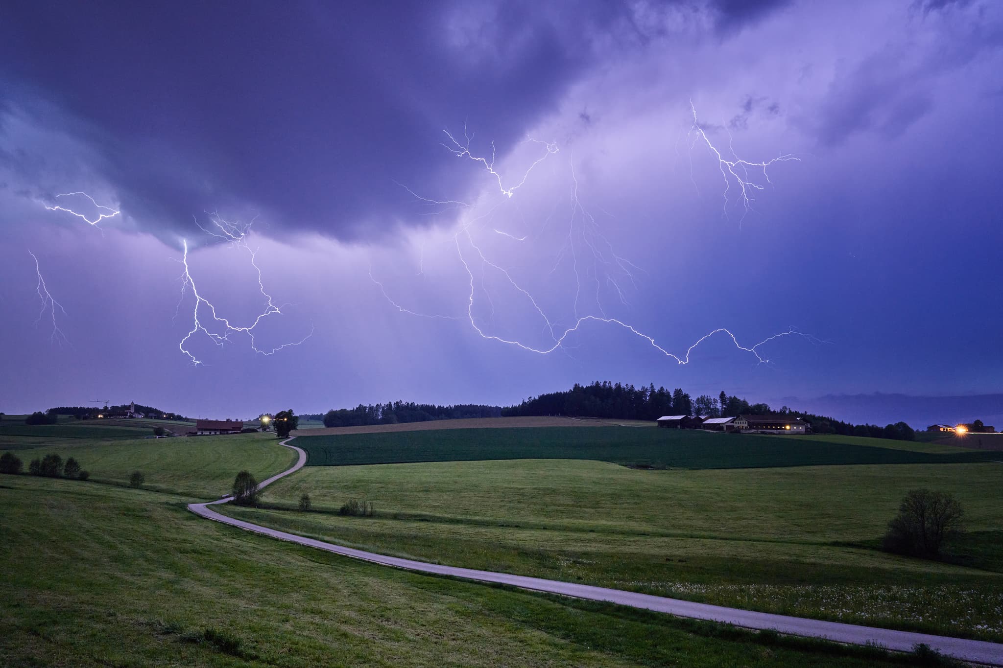 Gewitter um Ecking Arbing im Landkreis Altötting, Oberbayern, Region Inn-Salzach, Deutschland. Das Bild zeigt Blitze über Feldern und einer ländlichen Straße.