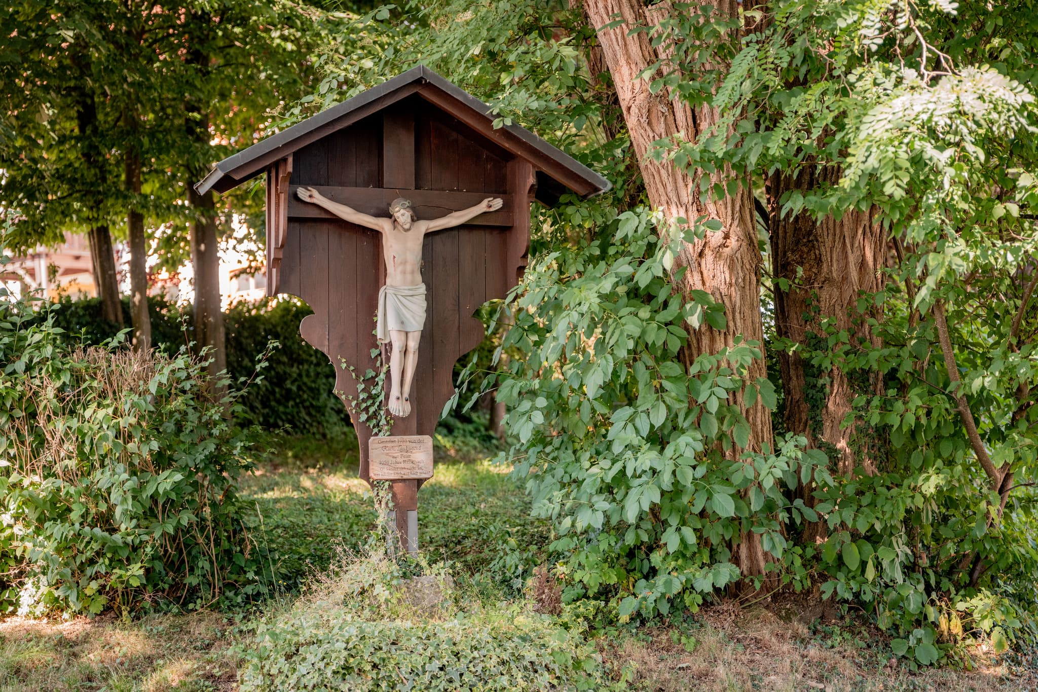 Holzwegekreuz der katholischen Landjugend in Reischach, Landkreis Altötting, Oberbayern, Region Inn-Salzach, Deutschland. Umgeben von Bäumen und Natur.