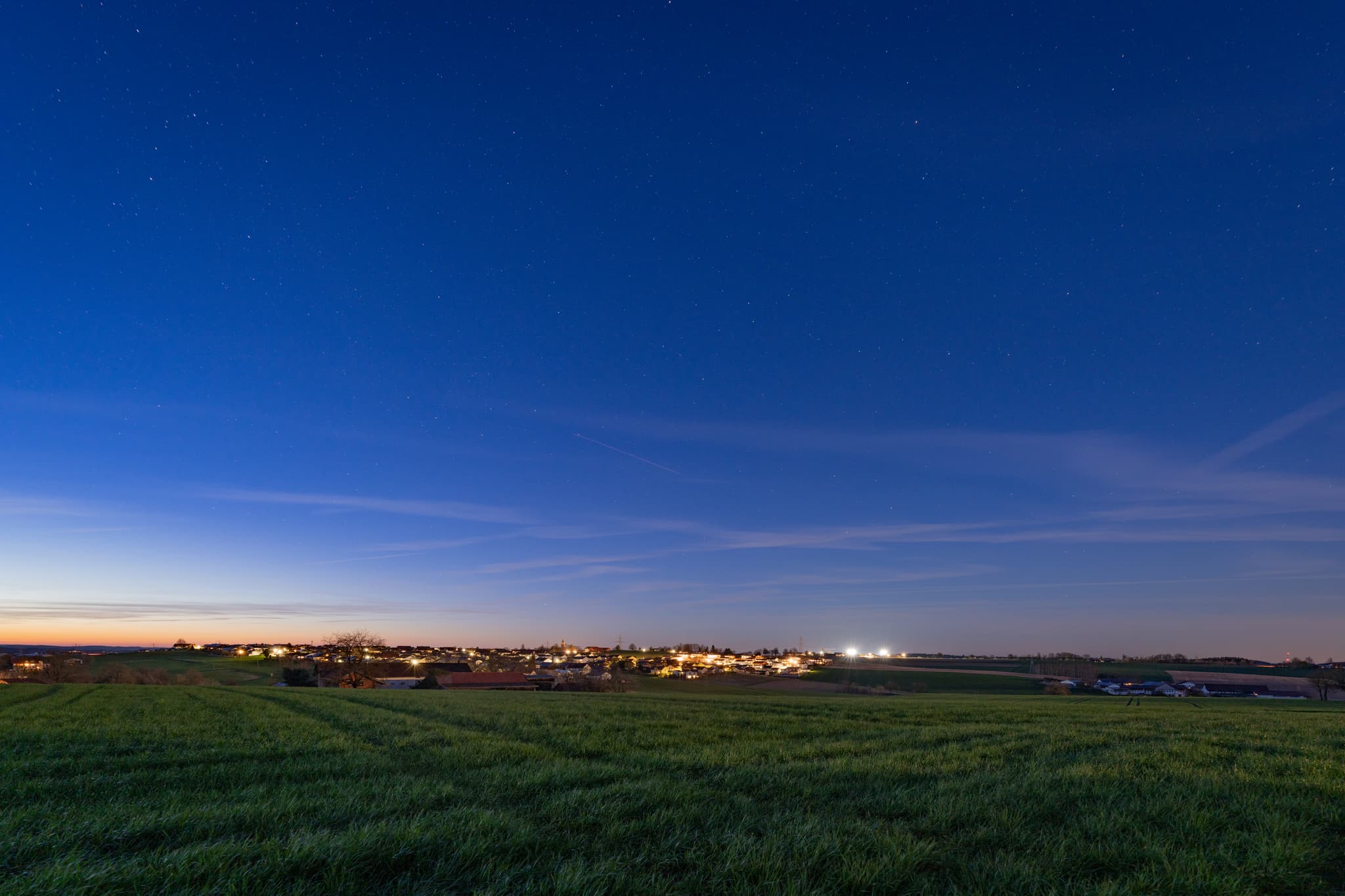 Vorleiten, Wurmannsquick, Landkreis Rottal-Inn, Niederbayern. Beleuchtete Gebäude in weitem Feldland unter klarem Sternenhimmel. Region Holzland, Deutschland.