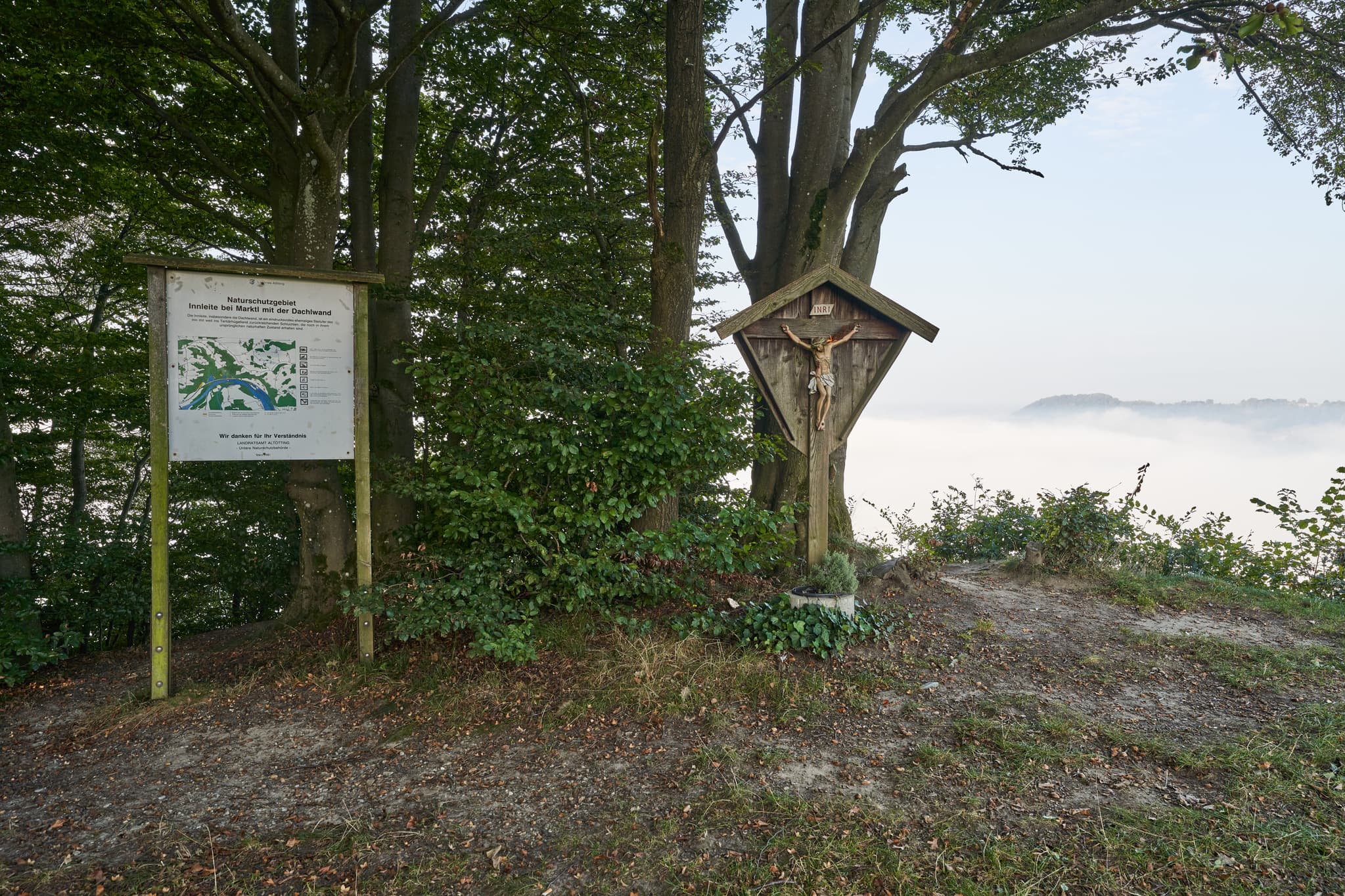 Morgendliche Aussicht über nebelverhangene Landschaft bei Marktl, Landkreis Altötting, Oberbayern. Kruzifix und Infotafel an der Aussicht. Inn-Salzach Natur.