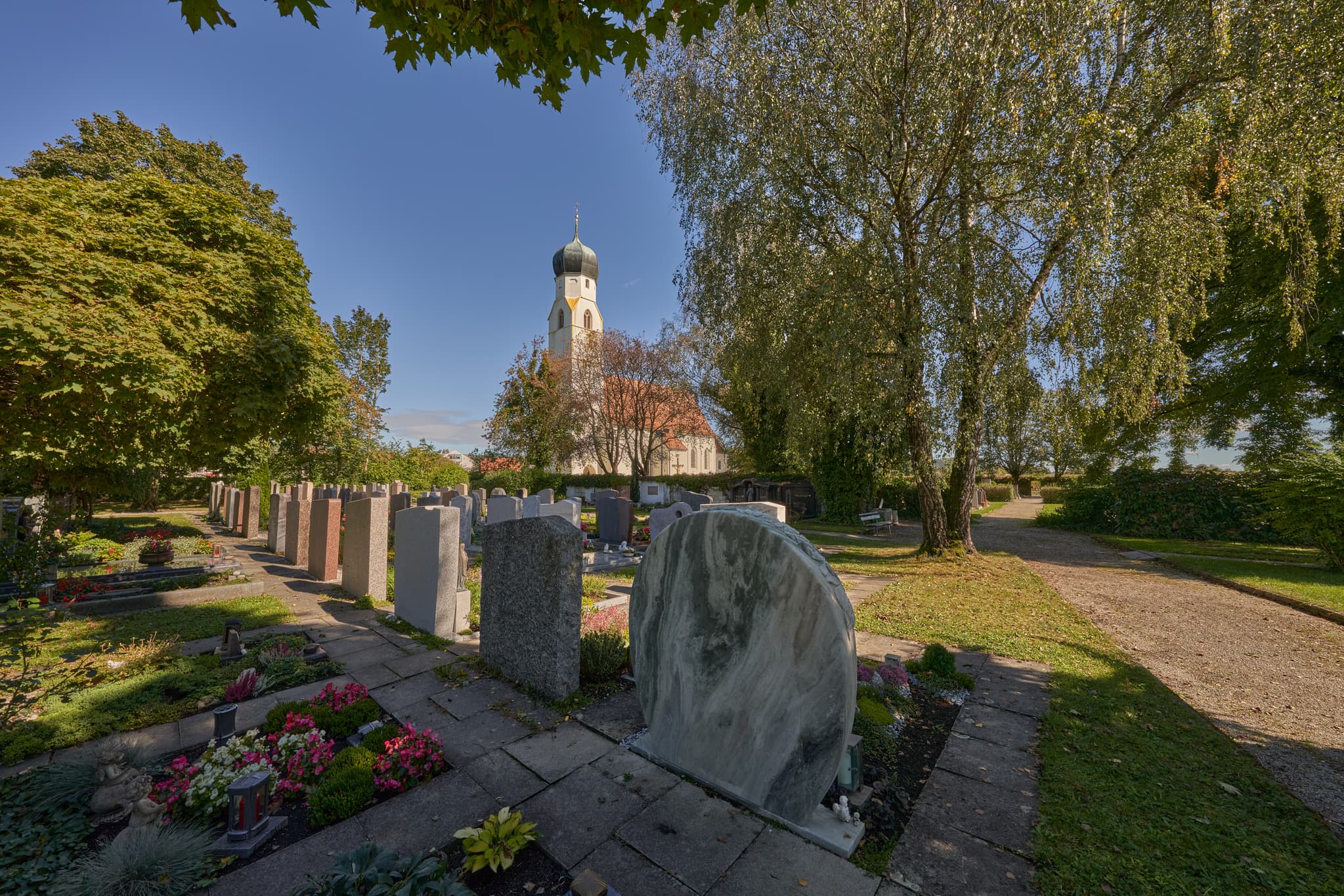 Die Kirche St. Maria in Winhöring, Landkreis Altötting, Oberbayern, zeigt sich umgeben vom Friedhof. Sakralarchitektur in der Region Inn-Salzach, Deutschland.