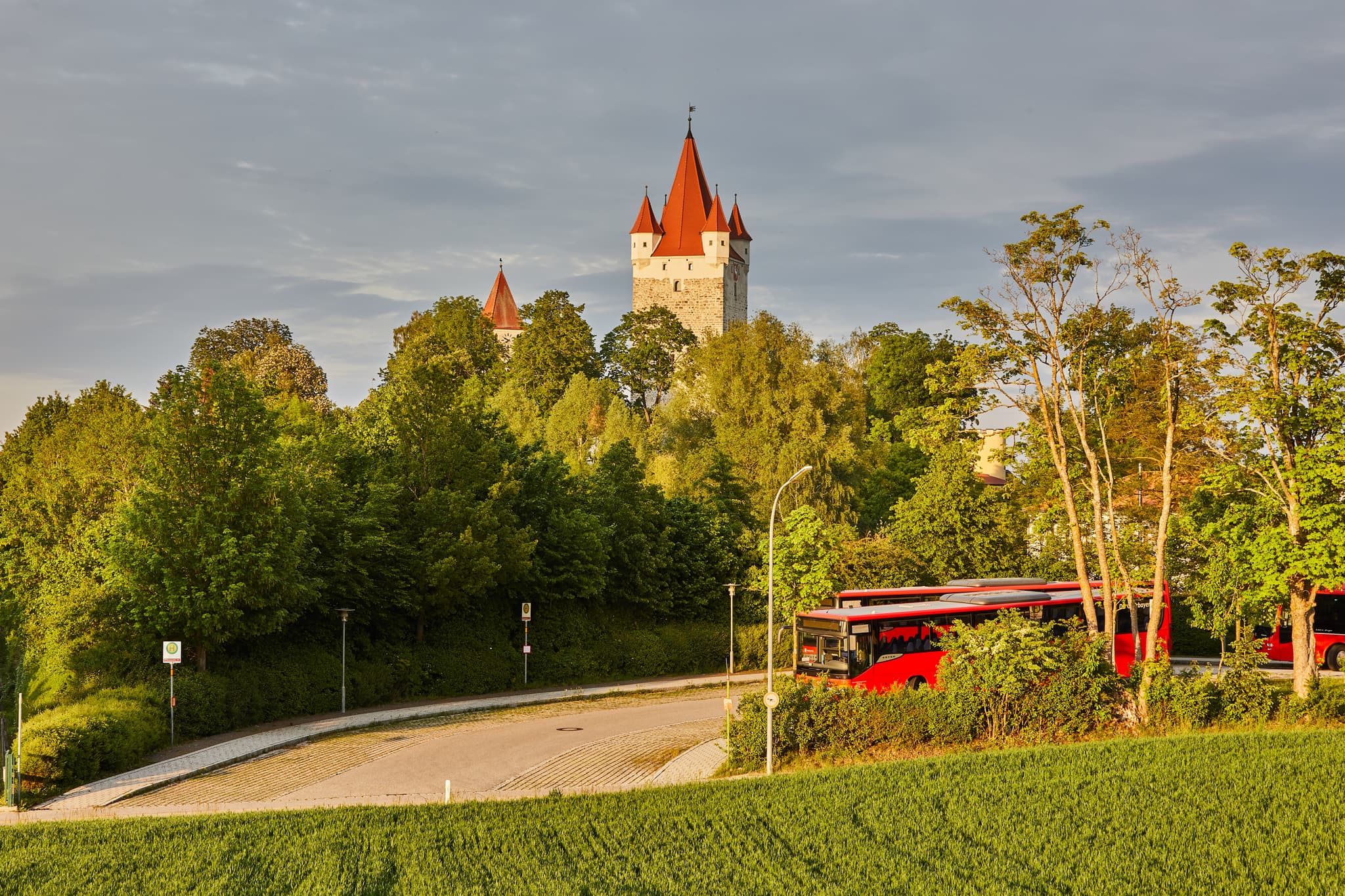 Schlossturm in Haag, Landkreis Mühldorf am Inn, Oberbayern. Bild mit Schlossturm, Bäumen, Straße und roten Bussen. Region Inn-Salzach, Deutschland.