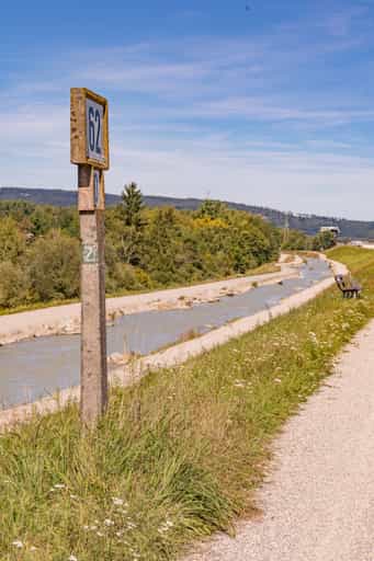 Inn-Radweg mit Uferzeichen, Bäumen, blauem Himmel.